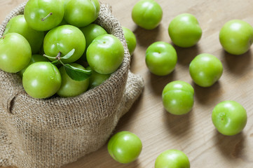 Fresh ripe organic green plums or greengage in burlap sack on wooden background, heap of may and june fruit, summer fruits concept