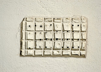metal grid cover with hole heap closeup on white stone wall, area diversity