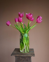 Bright pink tulip bouquet in a mason jar on a pedestal with terracotta background