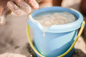 Kinderhand anblauem Plastik-Eimer, spielt im Sand am Strand