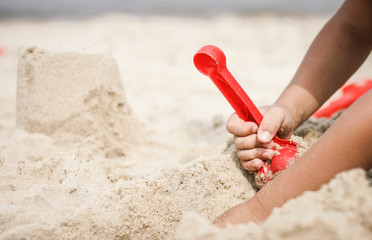 Kind spielt mit roter Schaufel am Strand und baut eine Sandburg