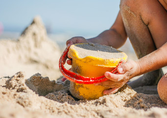 Kind hält spielt mit gelbem Plastik Eimer im Sand am Strand