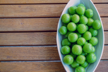 Green plums in white dish on wooden background close up view with copyspace