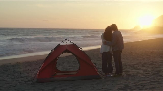 Couple enjoy sunset on ocean coast. Traveling on trailer and camping on beach. West coast of California. Lovely evening together.