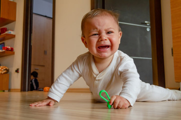 cute six months old baby boy having tummy time on the floor and crying for attention