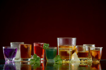 Fototapeta na wymiar Different alcoholic drinks in clear glasses with ice and mint on red background