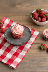 Homemade Strawberry Cupcakes; One Isolated on Stand; Fresh Strawberries in Bowl; Wooden Table