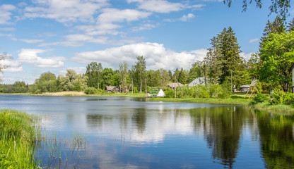 Fototapeta premium Scenic summer landscape with a lake surrounded by green forest. White clouds in the blue sky.