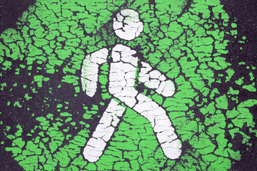 Background with white pedestrian icon on green. Cracked paint on asphalt. Go green and pedestrian priority concept