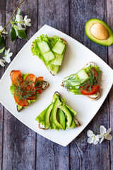 Vegetarian sandwiches with avocado, tomatoes and cucumbers on a wooden background
