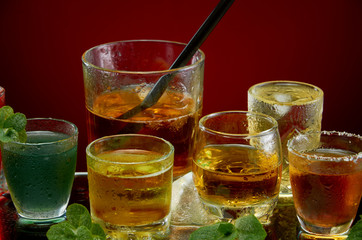 Glasses with various alcoholic drinks with ice and mint on red background