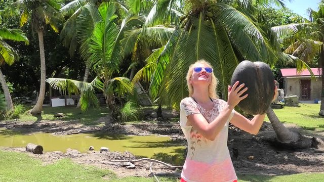 Tourist woman holding a female Lodoicea Maldivica nut known as sea coconut at Curieuse, Inner Islands, Seychelles. The coco de mer is endemic to Praslin and Curieuse. Sunny blue sky.