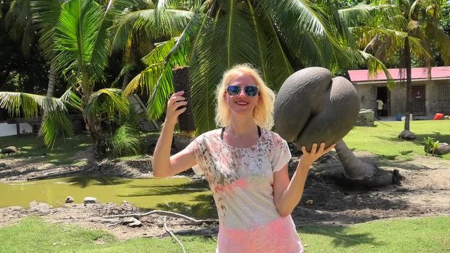 Happy fanny tourist woman holding Lodoicea Maldivica nut male and female, known as coco de mer or sea coconut at Curieuse Island in Seychelles. The coco de mer is endemic to Praslin and Curieuse.