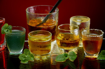Colored alcoholic drinks with ice and mint on red background