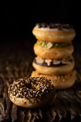 a piece of donut on wooden plank with a stack of donuts behind on dark background