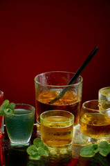 Colored alcoholic drinks with ice and mint on red background