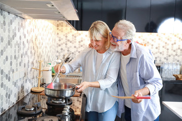 caucasian elderly wife making food in the kitchen with her caucasian elderly husband during his retirement life on table in happy holiday