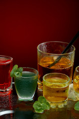 Colored alcoholic drinks with ice and mint on red background
