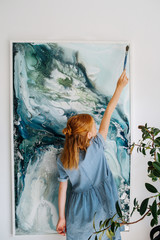 Teenage redhead girl is painting on a canvas hanging on the wall.