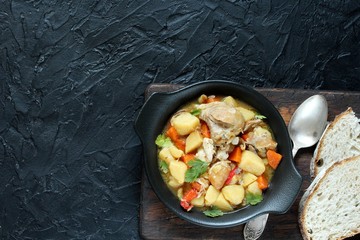 Chicken stew with potatoes and vegetables. in a black pan for serving dishes on a dark background surrounded by spices. meat and vegetables are pre-fried and then stewed. top view. copy space. 