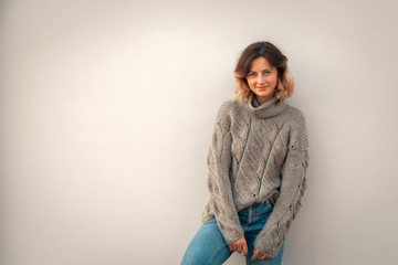  women and nature, peaceful mood, eco-friendly life.Young woman with a short haircut and in stylish clothes (knitted sweater and jeans) is smiling and posing against a white wall
