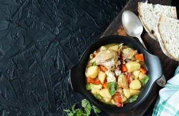 Chicken stew with potatoes and vegetables. in a black pan for serving dishes on a dark background surrounded by spices. meat and vegetables are pre-fried and then stewed. top view. copy space. 