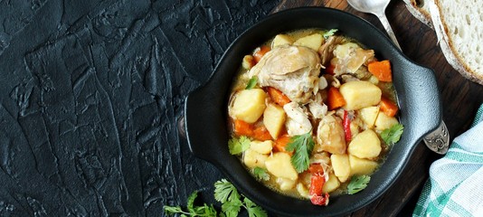 Chicken stew with potatoes and vegetables. in a black pan for serving dishes on a dark background surrounded by spices. meat and vegetables are pre-fried and then stewed. top view. copy space. 