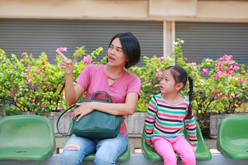 Asian mother and her daughter sitting at bus station. Mom and child girl passenger waiting for...
