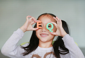 Happy little Asian child girl holding alphabet EQ (Emotional Quotient) text on her face. Education concept.