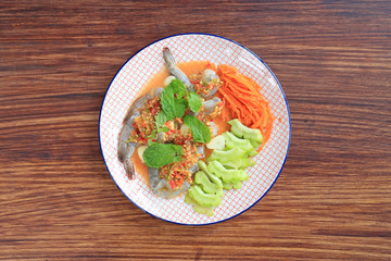 Delicious raw Shrimp in seafood chilli sauce with mint leaf and vegetables in plate on wooden table background. Top view.