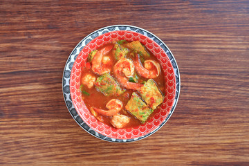 Delicious Thai yellow curry with shrimp and fried herb vegetable omelet in bowl on wooden table background. Top view.