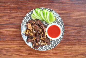 Deep fried beef served with sliced cucumber and sweet chili sauce on wooden board background.