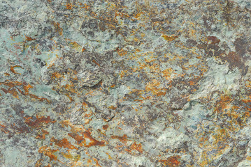 A rough piece of metal colored by pale green and orange corrosion.