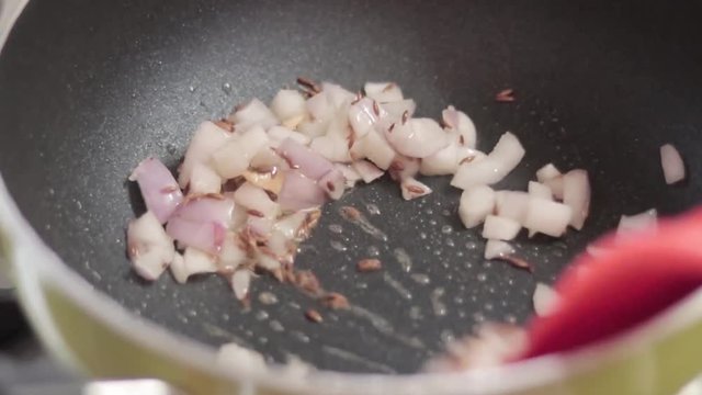 Cooking video of an onion and garlic in oll in a pan kept on a burning stove. Shot in natural soft lighting