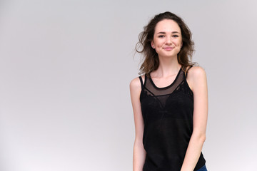 Fototapeta premium Life is a success. I am pleased with myself. Concept photo of a happy smiling woman satisfied life contented brunette girl in a black T-shirt and jeans on a gray background with flowing hair.