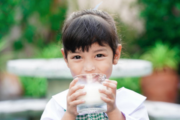 Asian cute student girl drinking a glass of milk at home before going to school in the morning. The concept is healthy and intelligent kid concept.    