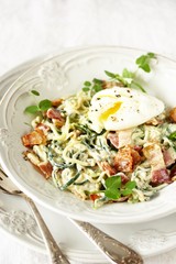 Low-Carb keto carbonara pasta with spaghetti (noodles) of zucchini with cream, fried bacon and poached egg. decorated with pea sprouts. in a beautiful light dish. recipes for fatty protein foods 