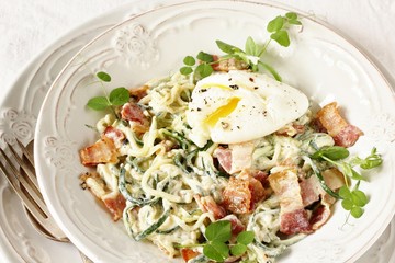 Low-Carb keto carbonara pasta with spaghetti (noodles) of zucchini with cream, fried bacon and poached egg. decorated with pea sprouts. in a beautiful light dish. recipes for fatty protein foods 