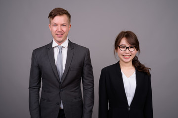 Young businessman and young Asian businesswoman against gray bac