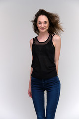 Life is a success. I am pleased with myself. Concept photo of a happy smiling woman satisfied life contented brunette girl in a black T-shirt and jeans on a gray background with flowing hair.