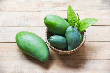 Green Mango summer fruit and green leaves in the basket on wooden background - Fresh raw mango