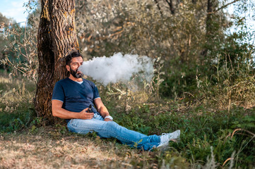 Naklejka na ściany i meble Bearded man blows up a couple an electronic cigarette on the forest ground. Getting rid of nicotine addiction.