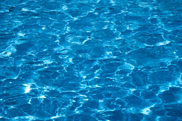 Blue and bright ripple water surface in swimming pool with sun reflection.
