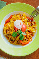 Top view of farfalle pasta with chicken and vegetables in a green plate. - 270143919