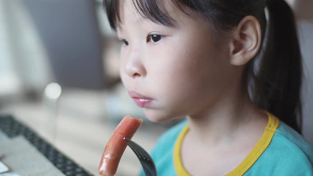 Little asian girl eating sausage for breakfast