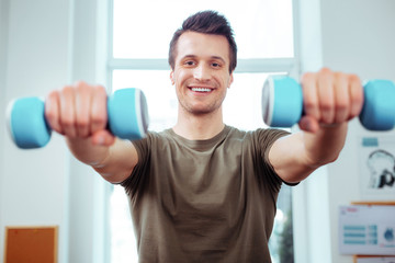 Happy positive man holding two blue dumbbells