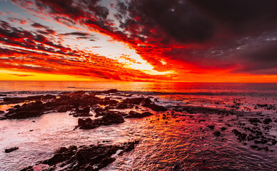 Dramatic nature landscape. Red sunset on the ocean shore. Beautiful sky. Shallow beach of the Pacific ocean
