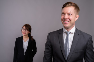 Young businessman and young Asian businesswoman against gray bac