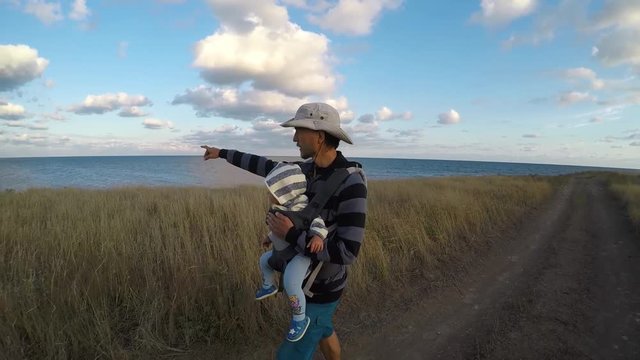Father and son in baby carrier are walking along the seashore. Family vacation. 