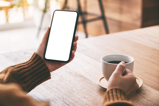 Mockup image of woman's hand holding black mobile phone with blank screen while drinking coffee
